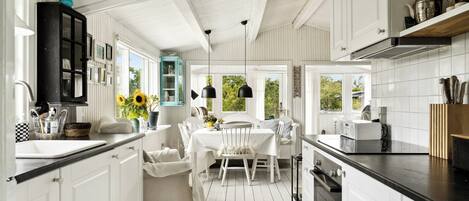 A kitchen with white cabinetry, a dining area with a white table and chairs, and a window with a view of greenery.