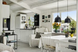 Un intérieur lumineux et blanc comprenant une cuisine, un coin repas et une vue sur l’extérieur.