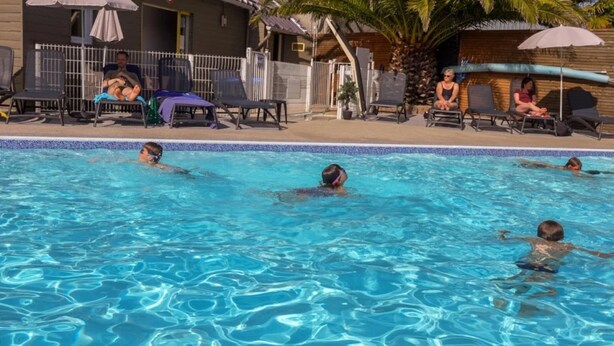 En swimmingpool med folk som simmar och solstolar runt poolområdet.
