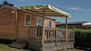 Eine Holzhütte mit Veranda, einem überdachten Bereich mit Streifenmarkise und einem kleinen Podest zum Eingang.