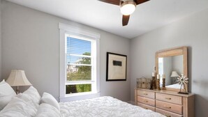 Una camera da letto con un letto, una cassettiera, un ventilatore a soffitto, una finestra e un quadro appeso al muro.