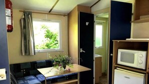 A compact kitchenette with a microwave, a small refrigerator, and a dining area with a table and bench. - Camping 3 étoiles - Piscine  - ccbgdcd (Rennes-les-Bains)