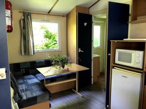 Eine kompakte Küchenzeile mit Mikrowelle, kleinem Kühlschrank und Essbereich mit Tisch und Bank.