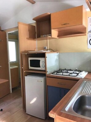 Una cocina compacta con microondas, refrigerador, estufa a gas y armarios de madera.