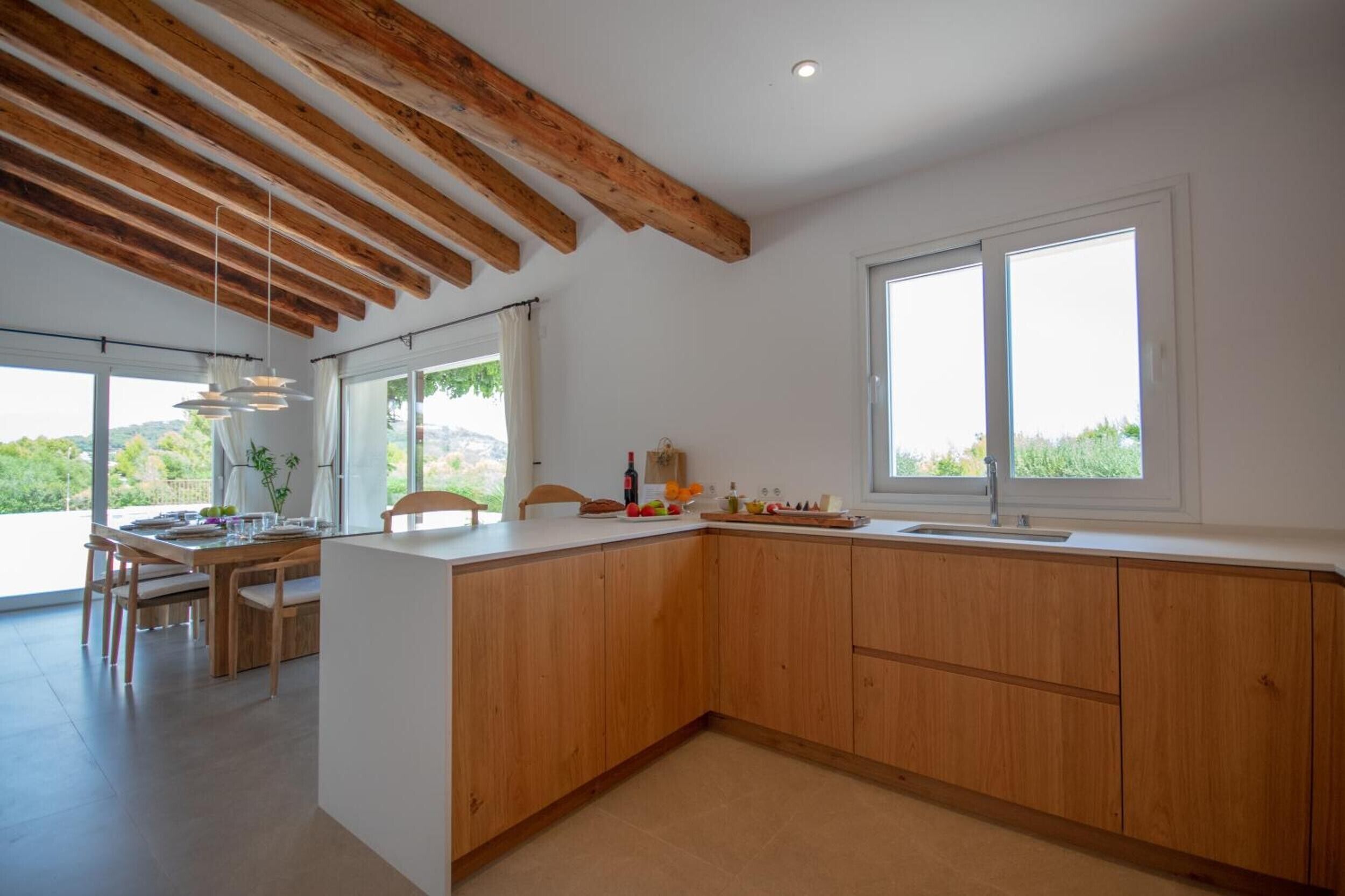 A modern kitchen with wooden beams, a dining area, and large windows.
