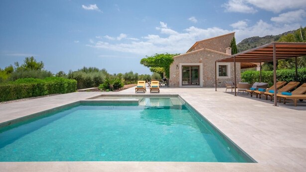 A swimming pool with lounge chairs, a stone building, and a view of the surrounding landscape.