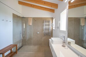 Un bagno moderno con doccia a parete in vetro, uno specchio grande e una panca in legno.