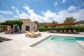 Area piscina con lettini, una zona relax coperta e un edificio in pietra con un'apertura.