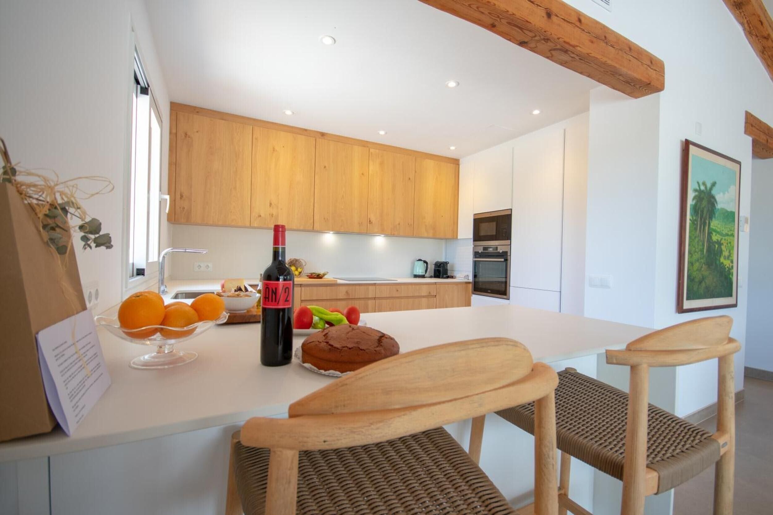 Een moderne keuken met houten kastjes, een wit aanrechtblad en een eethoek met twee houten stoelen.
