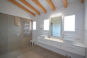 Uma casa de banho moderna com um espelho grande, duas pias, um porta-toalhas e um pequeno banquinho.