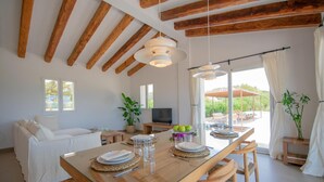 A dining area with a glass table, wooden chairs, and a television in the background.