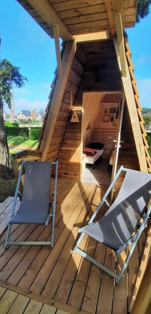 Eine Holzhütte mit geneigtem Dach, einer kleinen Küchenzeile und zwei Liegestühlen auf einer Holzterrasse.
