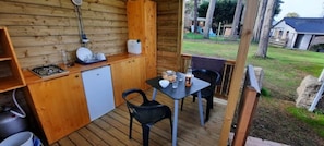 Une terrasse en bois avec une table et des chaises, un petit réfrigérateur et une cuisiniÚre à gaz.