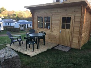 A wooden cabin with a deck, outdoor seating, and a door with windows.