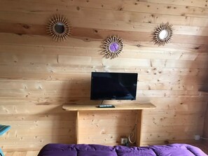 A room with wooden panel walls, a mounted television on a wooden stand, and a purple bedspread.