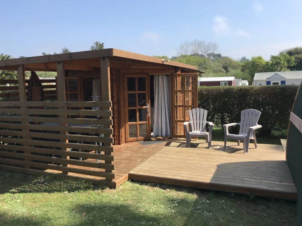 Una terraza de madera con dos sillas, una estructura de madera con una puerta y un área cercada.