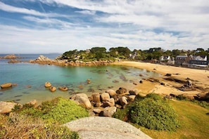 A coastal landscape with a sandy beach, clear water, and rocky outcrops.