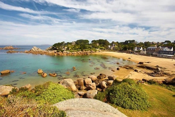 A coastal landscape with a sandy beach, clear water, and rocky outcrops.