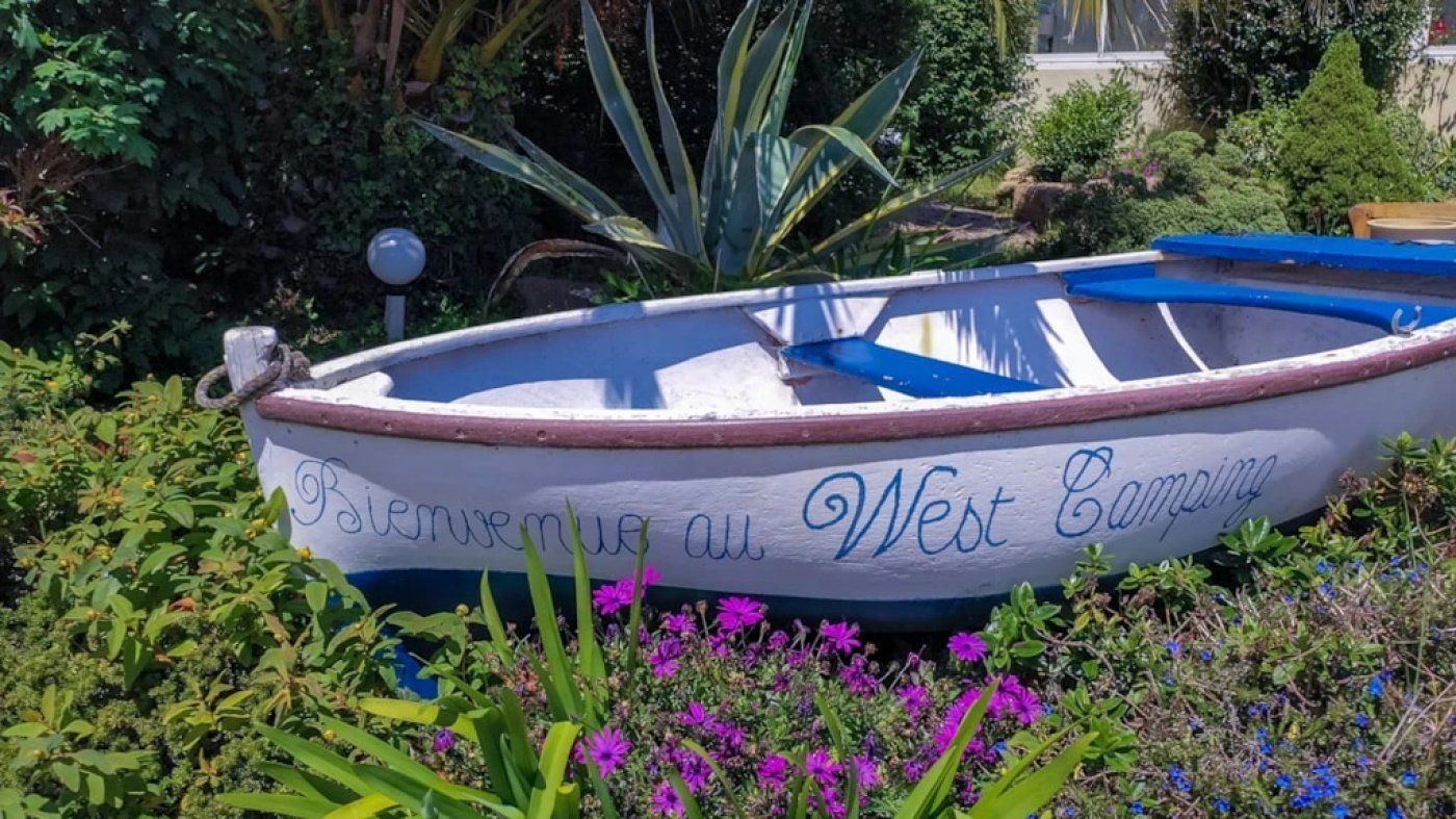 Un bote con la leyenda 'Rieserve au West Campan' escrito, rodeado de follaje y flores.