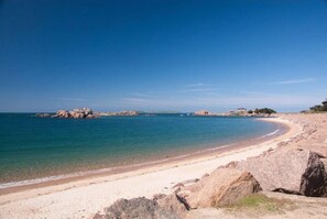 A beach with clear water, sandy shore, and rocky outcrops.