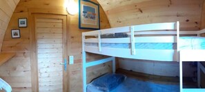 A wooden cabin interior with bunk beds, a door, and framed pictures on the wall.