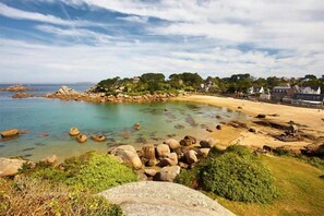 Paisaje costero con playa arenosa, agua cristalina y afloramientos rocosos.