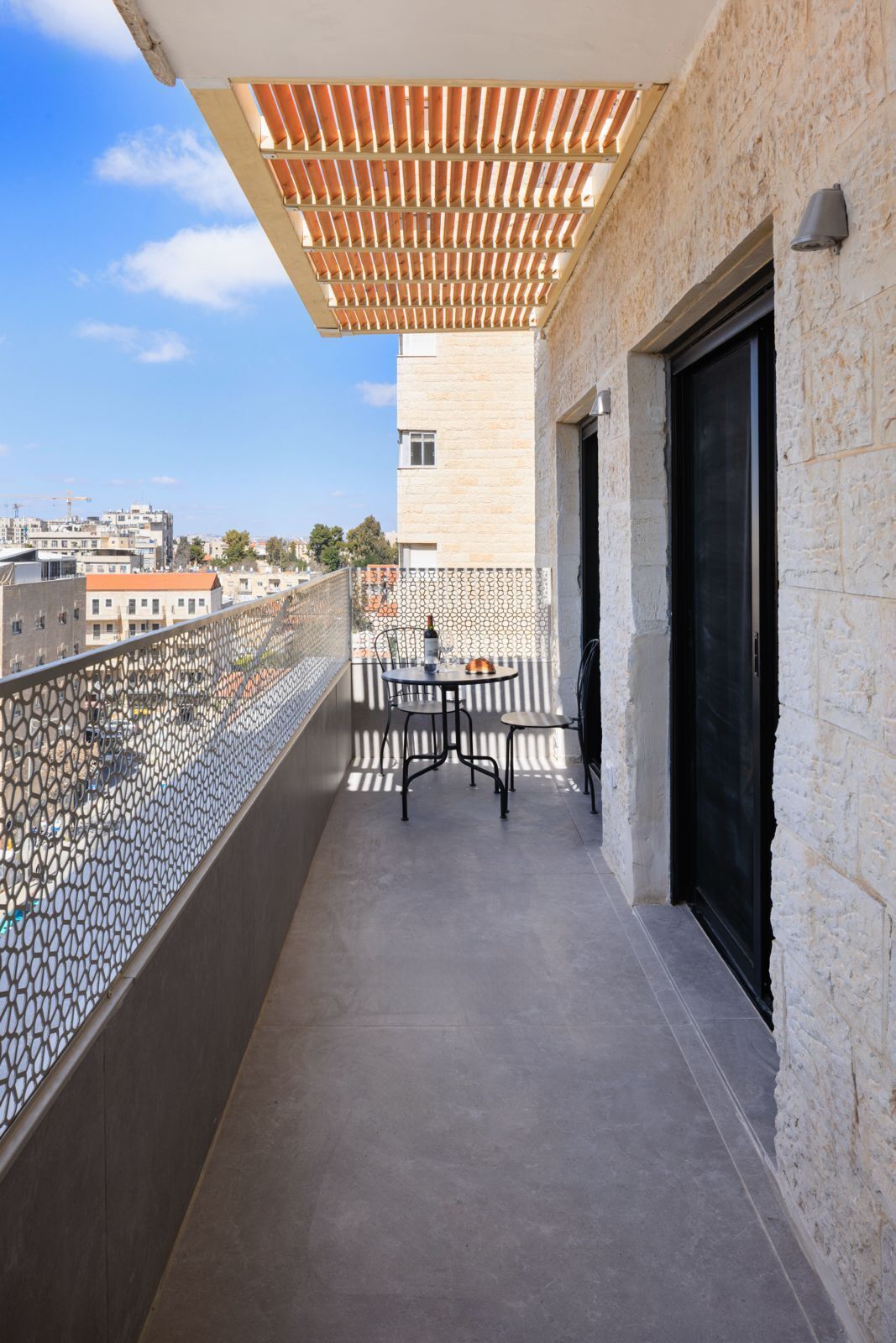 A balcony with a pergola, a table with chairs, and a view of the cityscape.