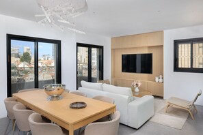 En moderne stue med spiseplads, sofa, fjernsyn monteret på væggen og en balkon med udsigt over byen.