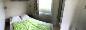 Ein kleines Zimmer mit einem Einzelbett, einem Fenster, einem Nachttisch und einem Vorhang.