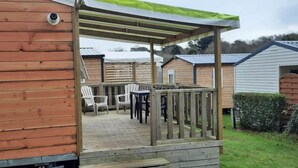 A wooden deck with a covered seating area and a small table. - Camping 3 étoiles - Piscine  - ccbgchf (Perros-Guirec)