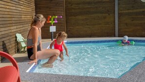A pool area with a wooden wall, a green chair, and a person in a striped swimsuit. - Camping 3 étoiles - Piscine  - ccbgchf (Perros-Guirec)