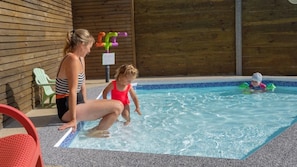 A pool area with a wooden wall, a green chair, and a person in a striped swimsuit. - Camping 3 étoiles - Piscine  - ccbgchf (Perros-Guirec)