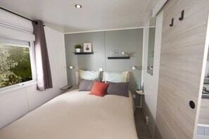 Ein Schlafzimmer mit Bett, einem Fenster mit Vorhängen, einem Nachttisch, einer Wandablage mit Pflanze und Bild.