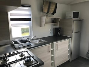 Eine kompakte Küche mit Gaskochfeld, Spüle, Mikrowelle und Kühlschrank.