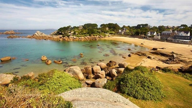 Ett kustlandskap med en sandstrand, klart vatten och klippiga utskjutande partier.