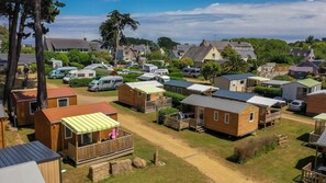 A campsite with multiple wooden cabins, some with attached porches, and a few with attached vehicles. - Camping 3 étoiles - Piscine  - ccbgchh (Perros-Guirec)