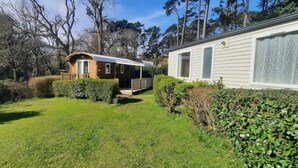Uma casa móvel com varanda, rodeada por um gramado bem cuidado e árvores densas.