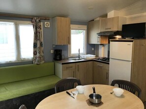 A compact kitchen with a dining table, chairs, a stove, and a refrigerator. - Camping 3 étoiles - Piscine  - ccbgci0 (Perros-Guirec)