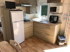 A compact kitchen with a refrigerator, microwave, stove, sink, and a small trash bin. - Camping 3 étoiles - Piscine  - ccbgcia (Perros-Guirec)