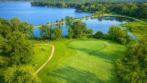A golf course with a water body, trees, and a clear sky.