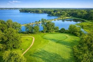 A golf course with a water body, trees, and a clear sky.