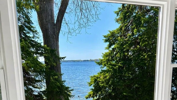 A window with a view of a lake surrounded by trees.