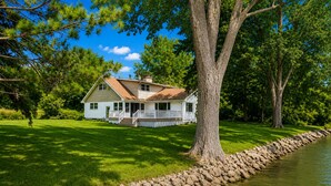 A house with a porch, a stone retaining wall, and a pond.