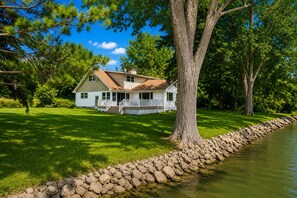 A house with a porch, a stone retaining wall, and a pond.