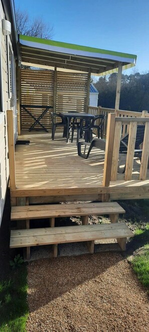 Eine Holzterrasse mit Außenmöbeln, einem überdachten Bereich und einer Holztreppe zu einem Gebäude.