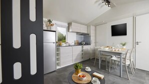Een moderne keuken met witte kastjes, een eettafel met stoelen en een kleine ronde tafel met een plant en een schaal fruit.