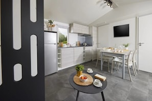 Eine moderne Küche mit weißen Schränken, einem Esstisch mit Stühlen und einem kleinen runden Tisch mit Pflanze und Obstschale.