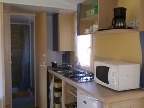 A compact kitchen with a gas stove, a microwave, and a coffee maker on the countertop. - Camping 3 étoiles - ccbgdg0 (Neuwiller-lès-Saverne)