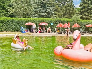 A swimming pool with inflatable flamingo floats, surrounded by greenery and umbrellas. - Camping 3 étoiles - ccbgdg0 (Neuwiller-lès-Saverne)