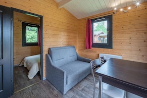 A cozy cabin interior with a sofa, a small table, and a window with a view of a house.